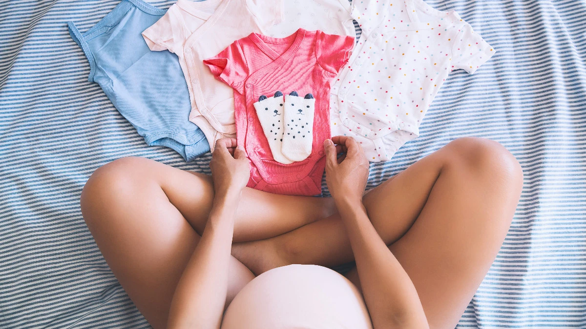 Babykleidung und Babybauch Frau mit Babybauch schaut sich Babykleidung an
